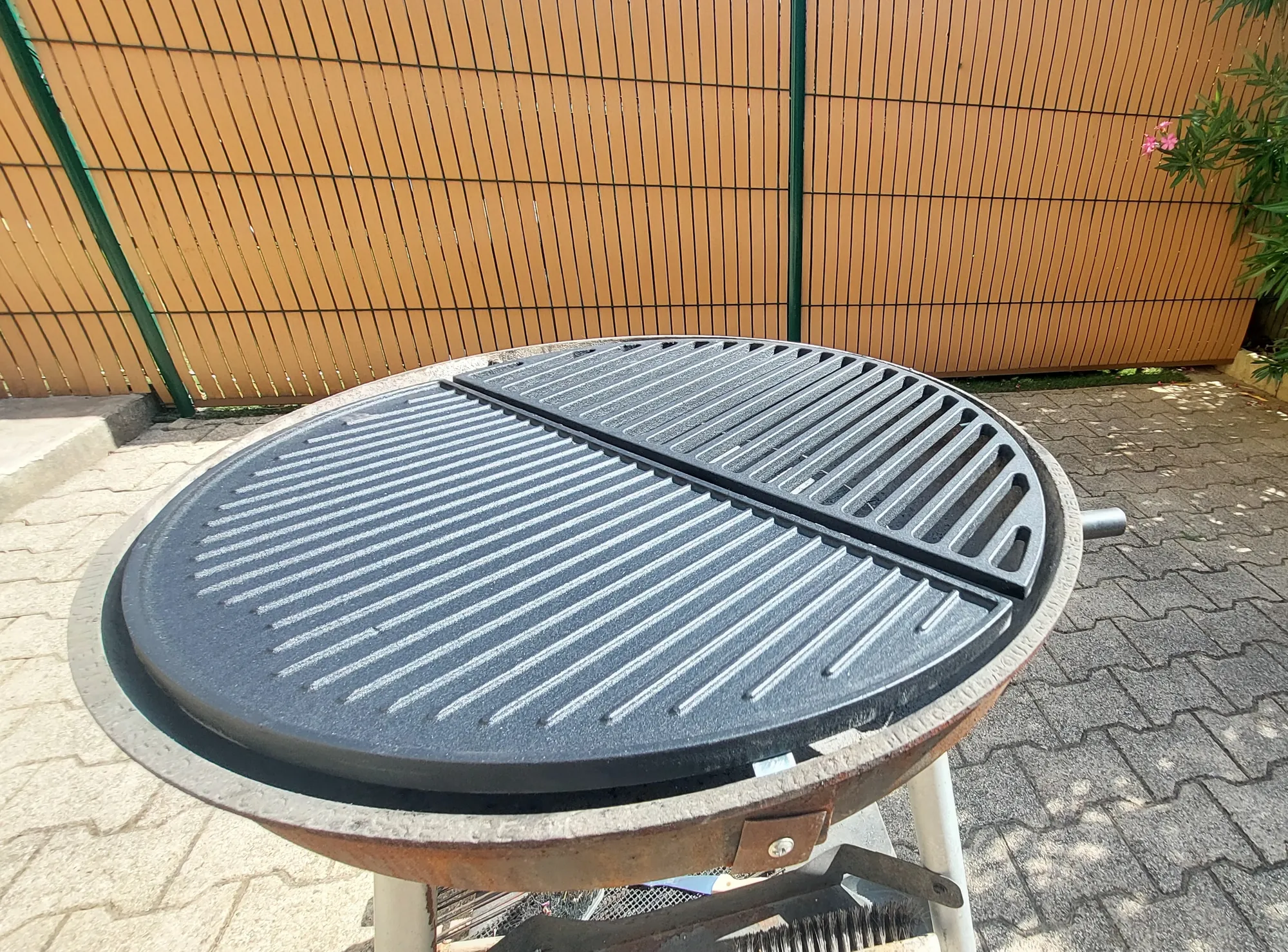 Le barbecue à charbon rond, avec sa plancha et sa grille en fonte, sur un sol pavé