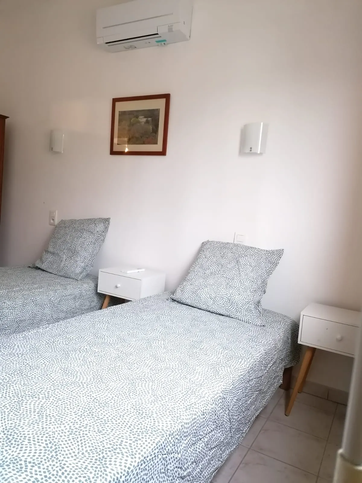 Deux lits simples séparés par une table de nuit, sous un climatiseur mural