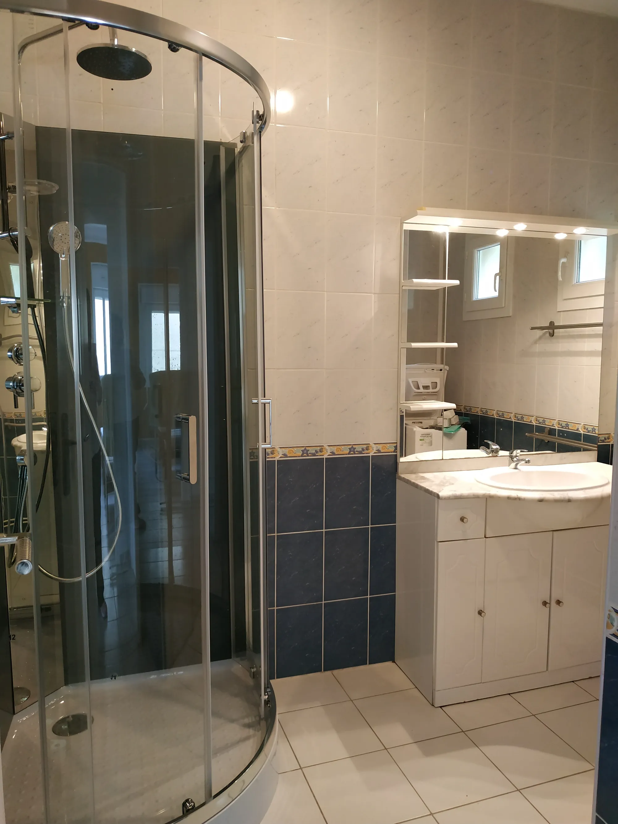 Salle de bains avec cabine de douche arrondie, meuble vasque et grand miroir