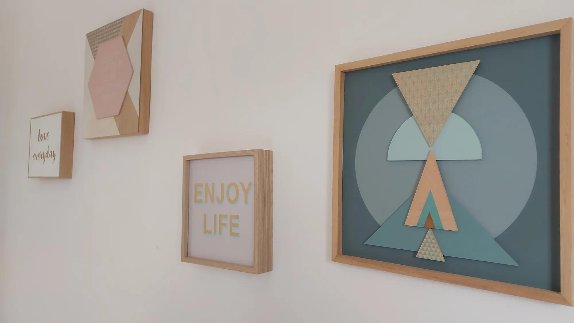 Trois cadres décoratifs aux motifs géométriques pastel accrochés à un mur blanc